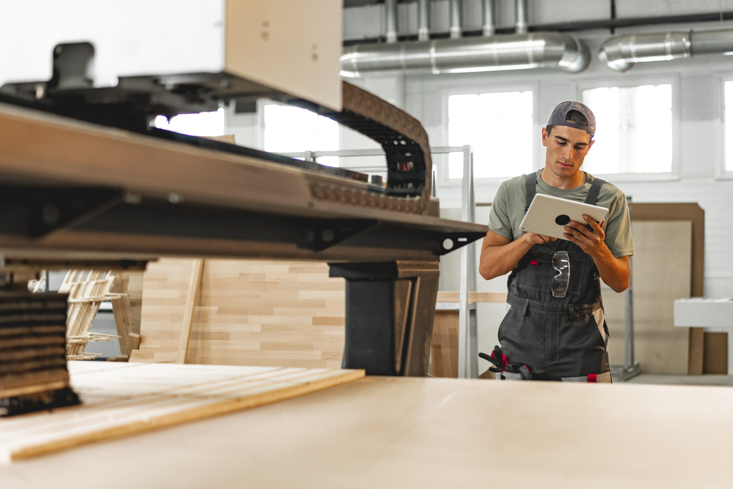 Young carpenter operating machine for wood processing at a furniture factory Jeune charpentier opérant une machine de transformation du bois dans une usine de meubles